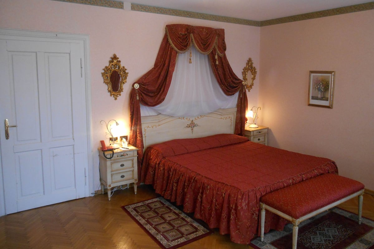 Ein Schlafzimmer mit einem großen Bett, zwei Nachttischen, einem Beistelltisch, einem Spiegel und einer Tür.
