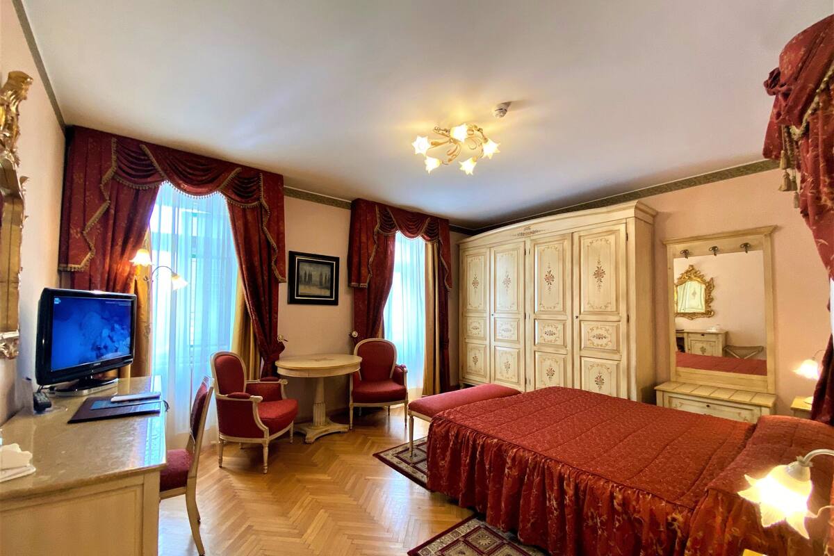 Ein Hotelzimmer mit einem Bett, einem Schreibtisch mit Computer, einem Stuhl, einem Kleiderschrank und einem Fernseher.