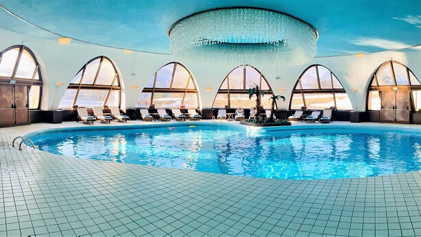 Ein großer, überdachter Pool mit Bogenfenstern und gefliestem Boden.