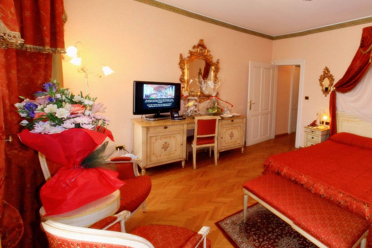 Ein Hotelzimmer mit einem großen Bett, einem Schreibtisch mit Computer, einem Sessel, einem Spiegel und einem roten Vorhang.