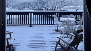 Ein mit Schnee bedeckter Balkon mit Gartenmöbeln, Blick auf verschneite Berge und einen klaren Himmel.