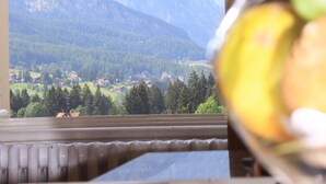 Blick durch ein Fenster auf eine Berglandschaft, ein Heizkörper und ein Glasbehälter mit Äpfeln.