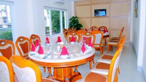A dining area with a round table set for a meal, surrounded by orange and white chairs. - Tecco Sky Hotel (Thanh Vinh)