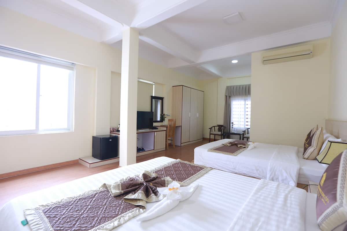 A hotel room with two beds, a desk, a chair, a wardrobe, and an air conditioning unit.