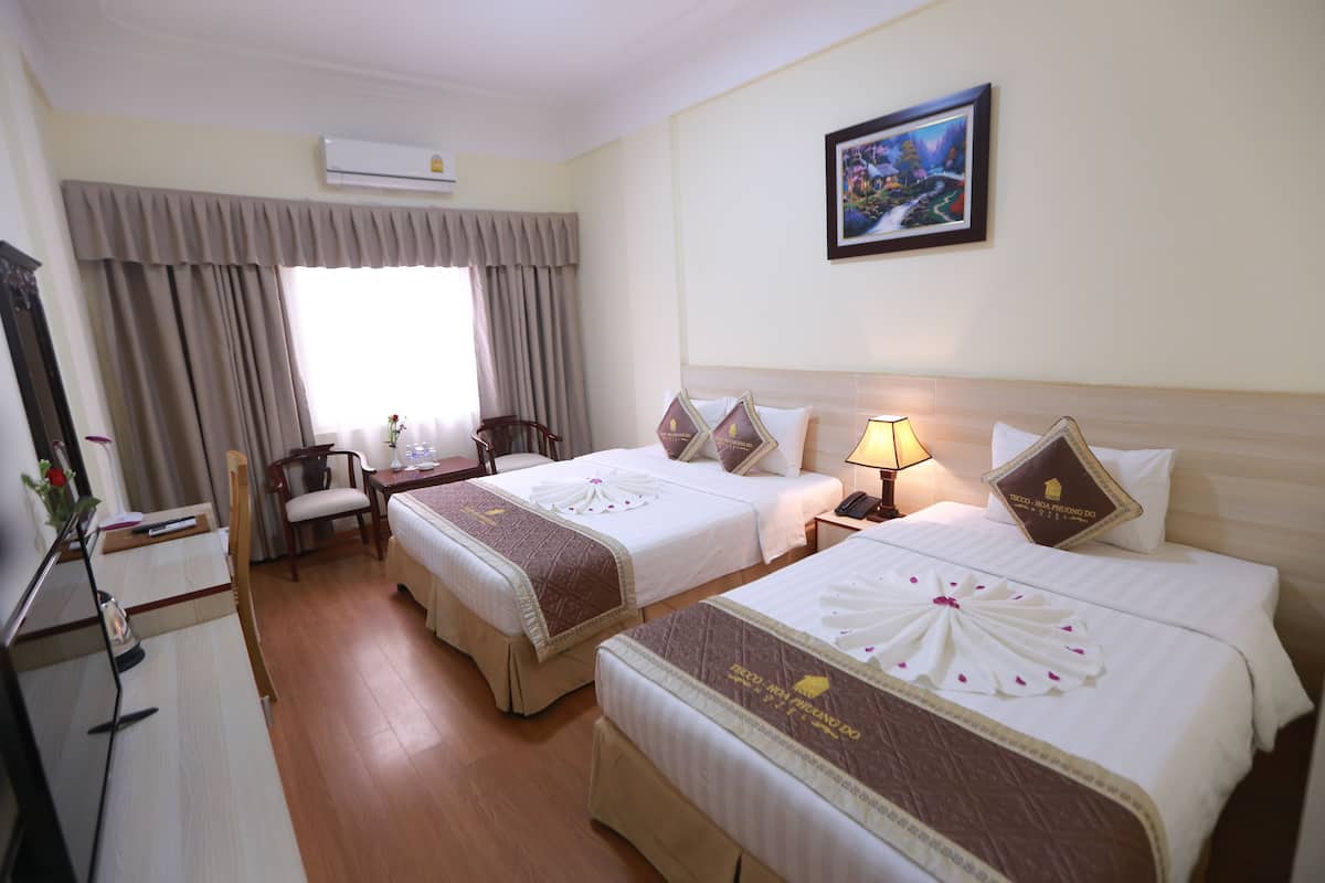 A hotel room with two beds, a desk, a chair, a desk lamp, and a painting on the wall.