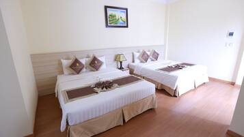 A hotel room with two beds, each with a brown decorative pillow, a bedside lamp, and a framed picture on the wall.