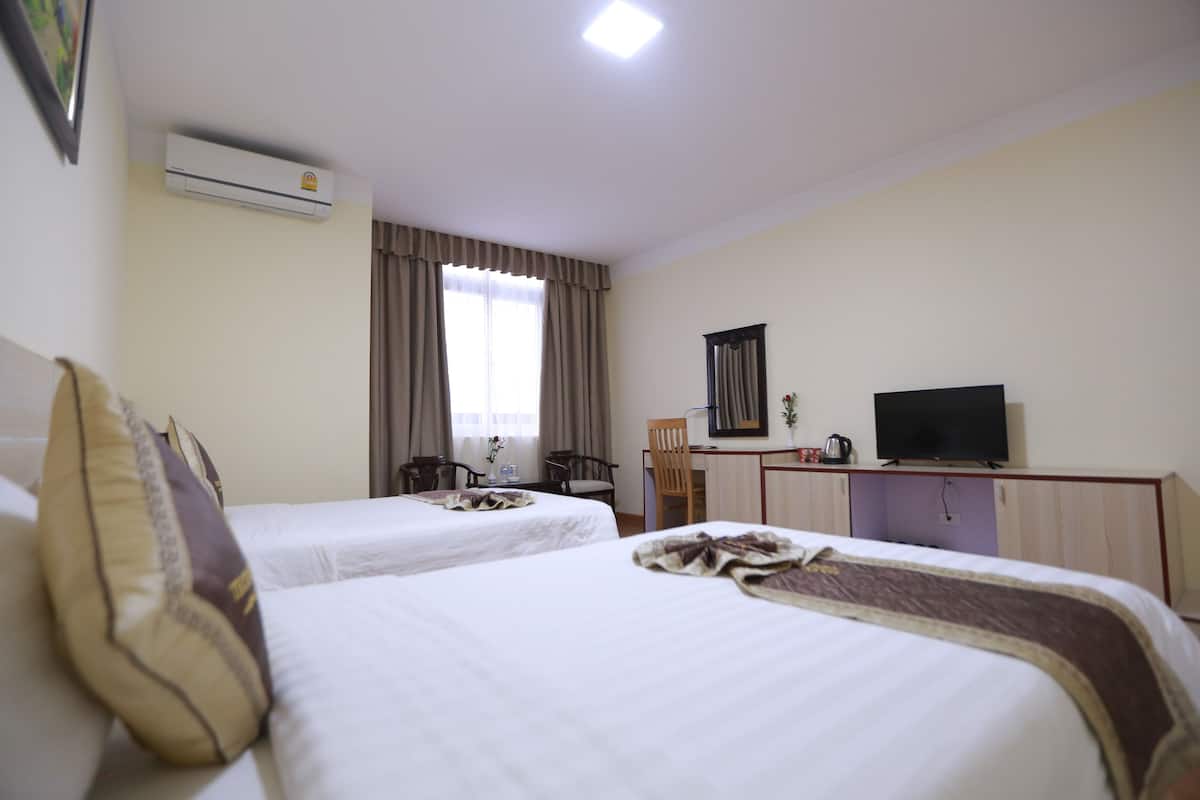 A hotel room with two beds, a desk with a television, and an air conditioning unit.
