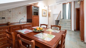 A modern kitchen with wooden cabinets, a built-in oven, and a dining area with a wooden table and chairs. - Villa Meri (Trogir)