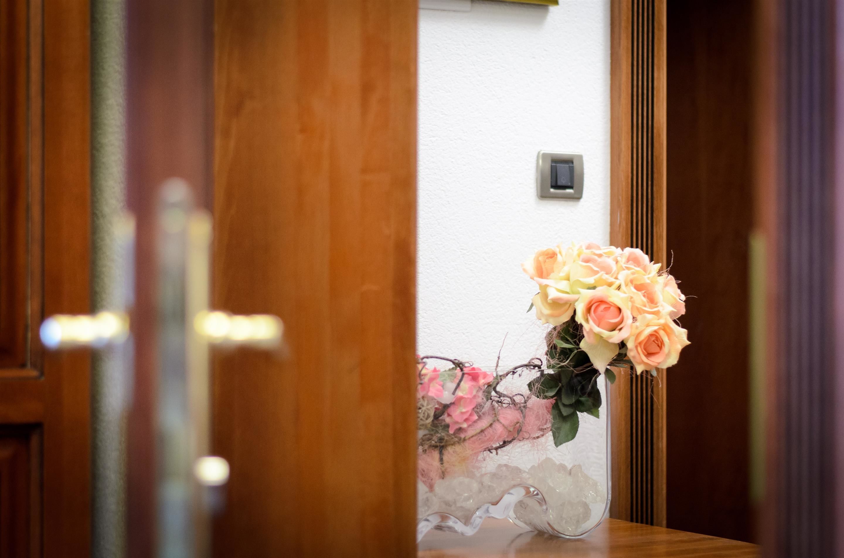 Une porte en bois avec un panneau de verre, un mur blanc et un vase rempli de roses.