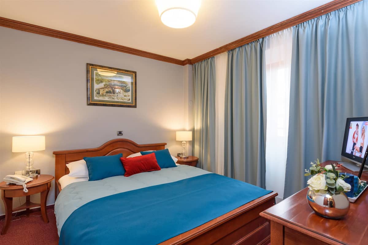 A hotel room with a large bed, two bedside tables, a TV, and a framed picture on the wall.