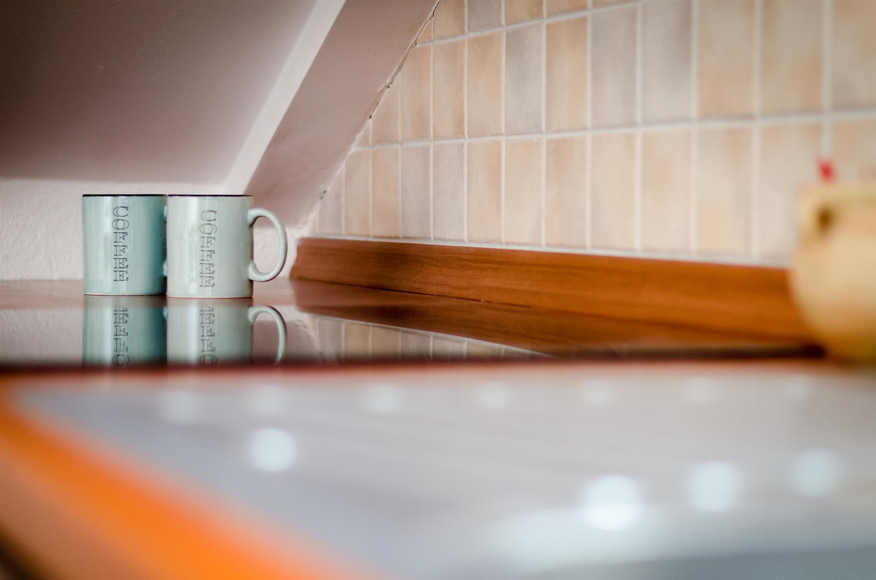 Een keuken met een betegelde spatwand, een houten aanrechtblad en twee witte mokken met de tekst 'COFFEE' erin gegraveerd.