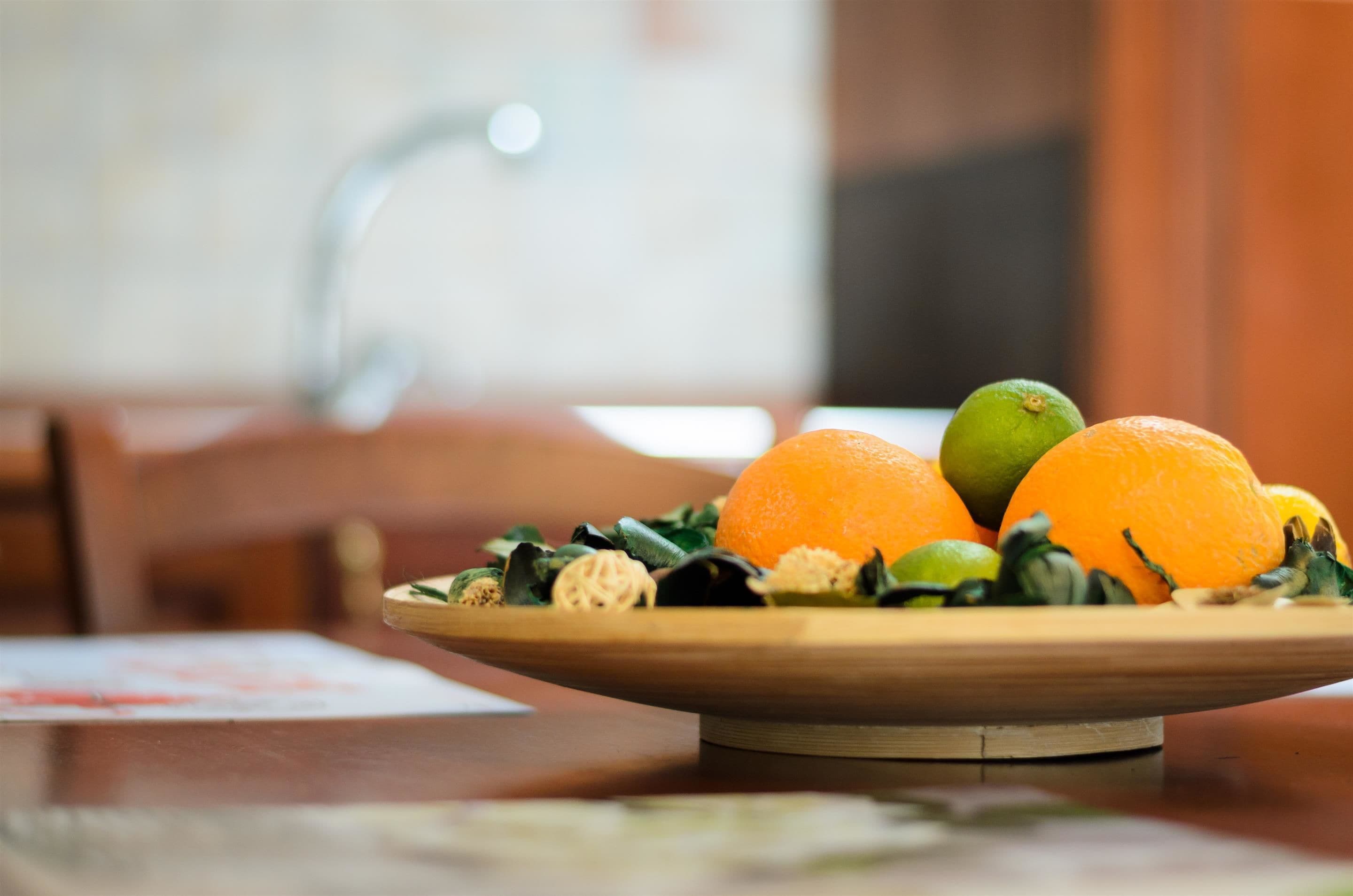 A wooden plate with oranges and a lime on a table.