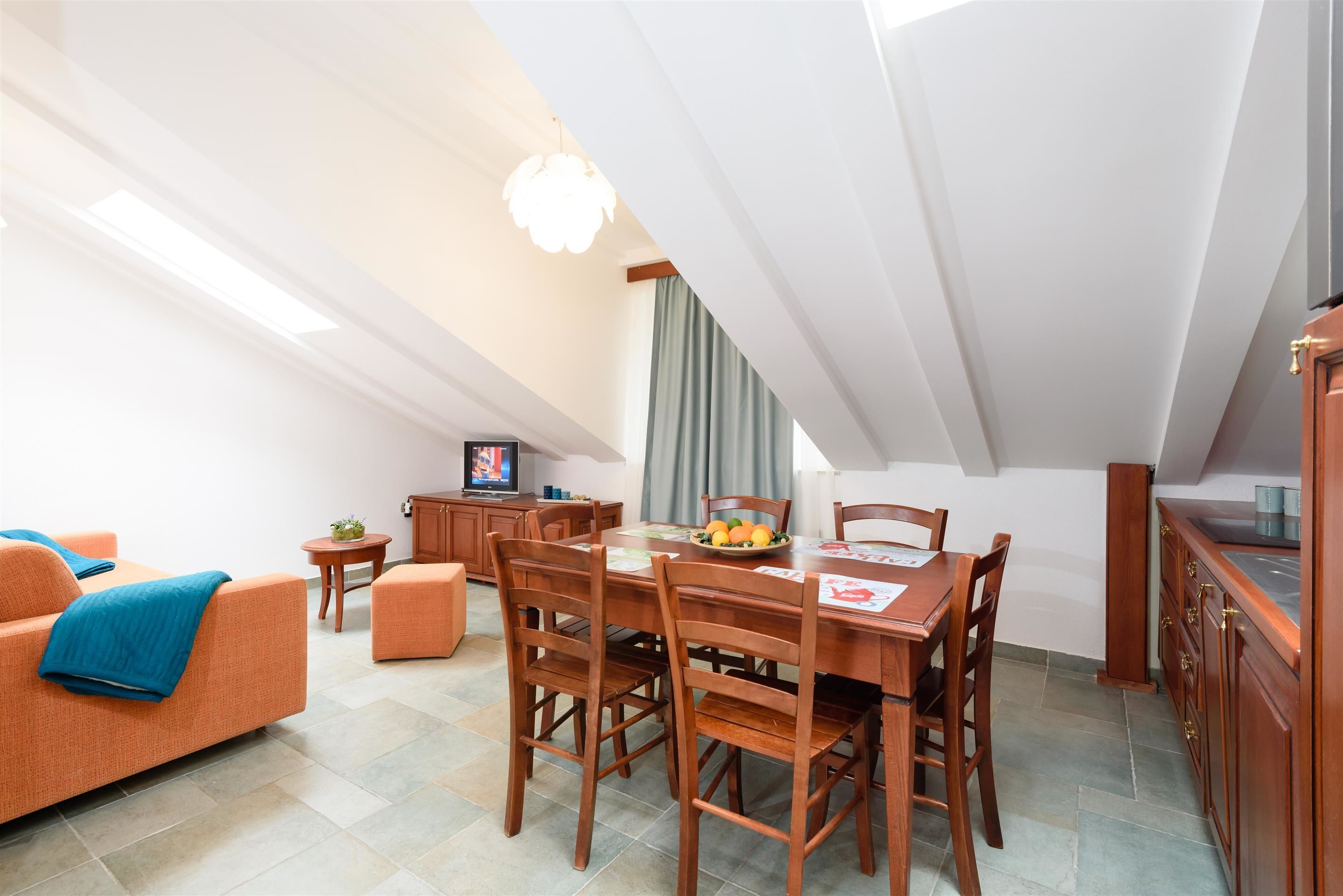 A dining area with a wooden table and chairs, a small side table, and a television in the background.