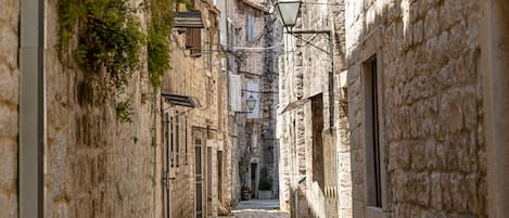 Un estrecho camino empedrado flanqueado por edificios históricos de piedra con balcones y un farol.