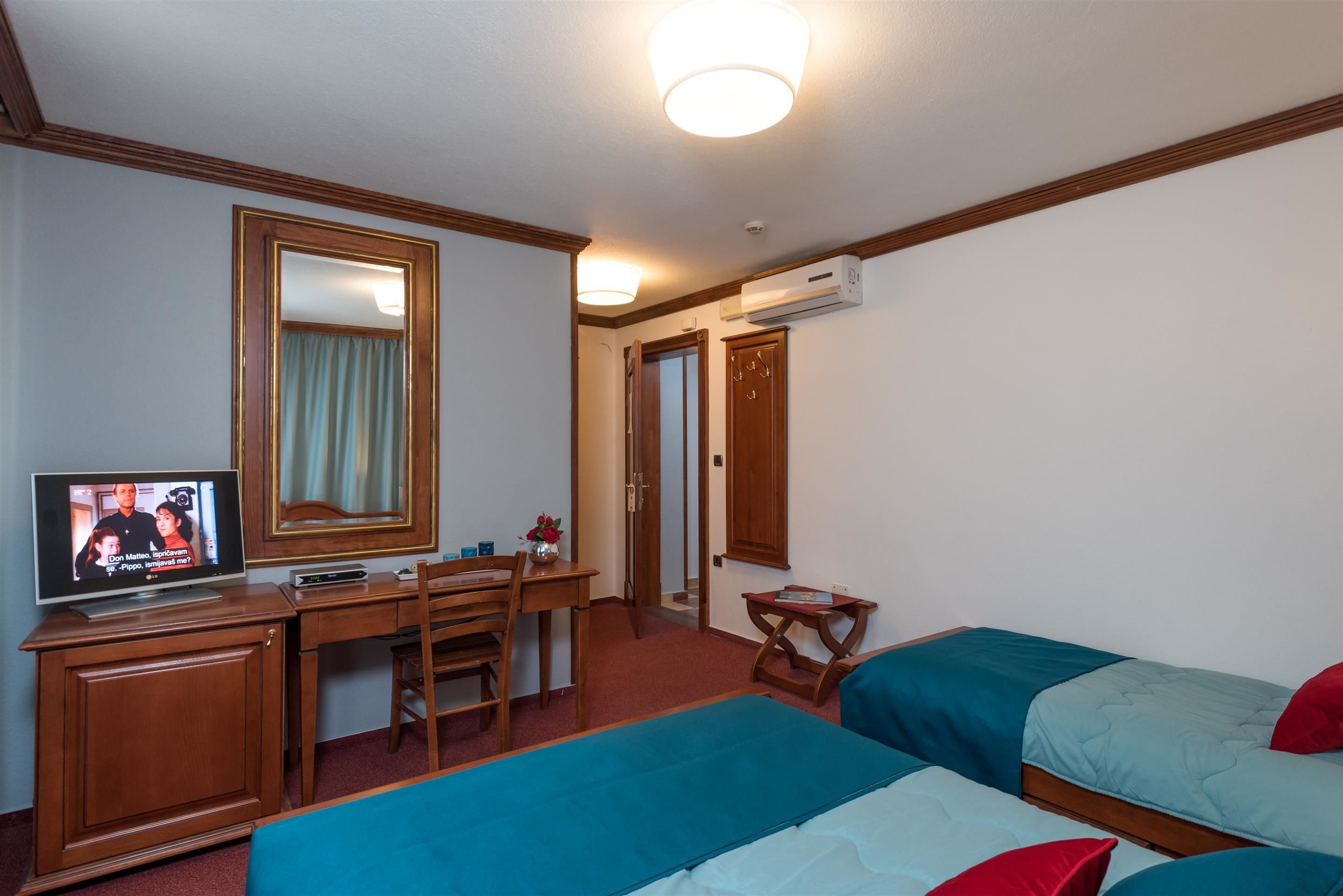 Een hotelkamer met een bed, een bureau met een televisie, een stoel en een klein tafeltje met een vaas.