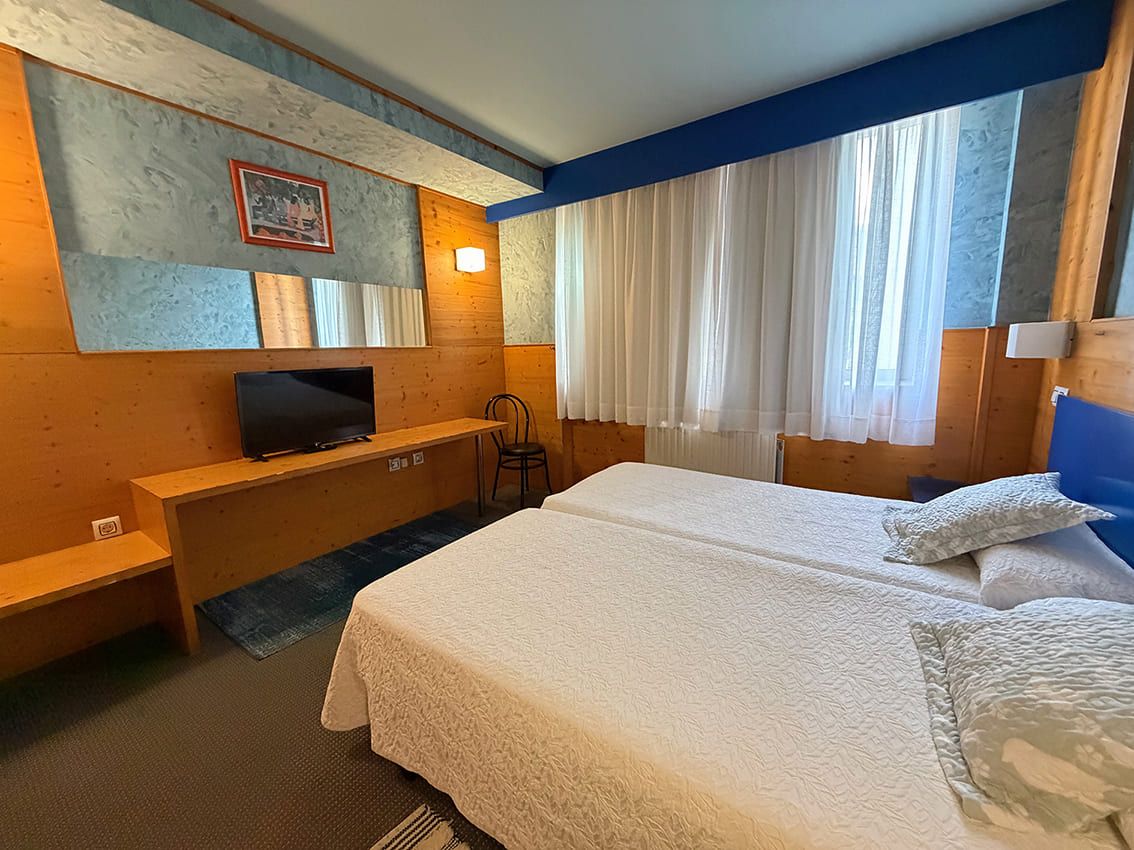 Una habitación de hotel con cama, televisor, escritorio y ventana con cortinas.