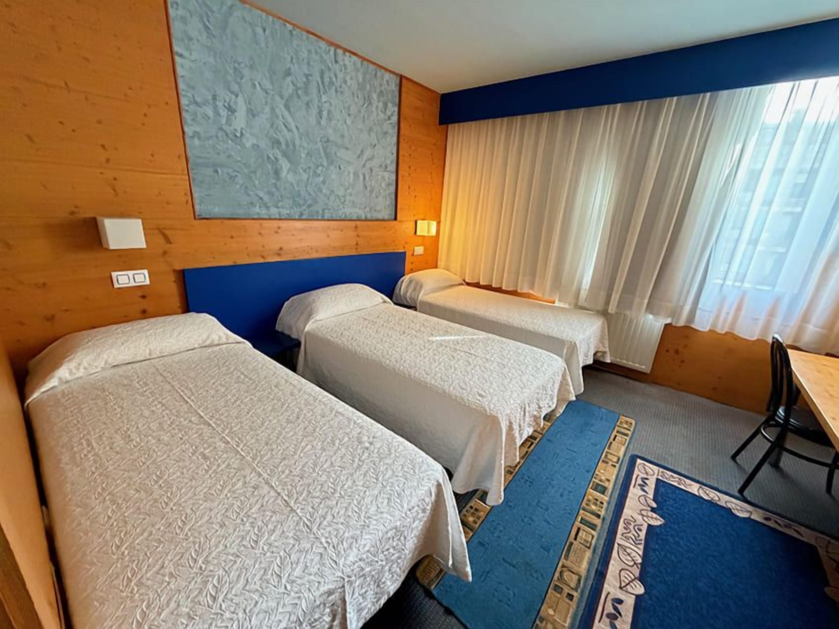 Une chambre d’hôtel avec deux lits, un bureau et une fenêtre avec des rideaux.