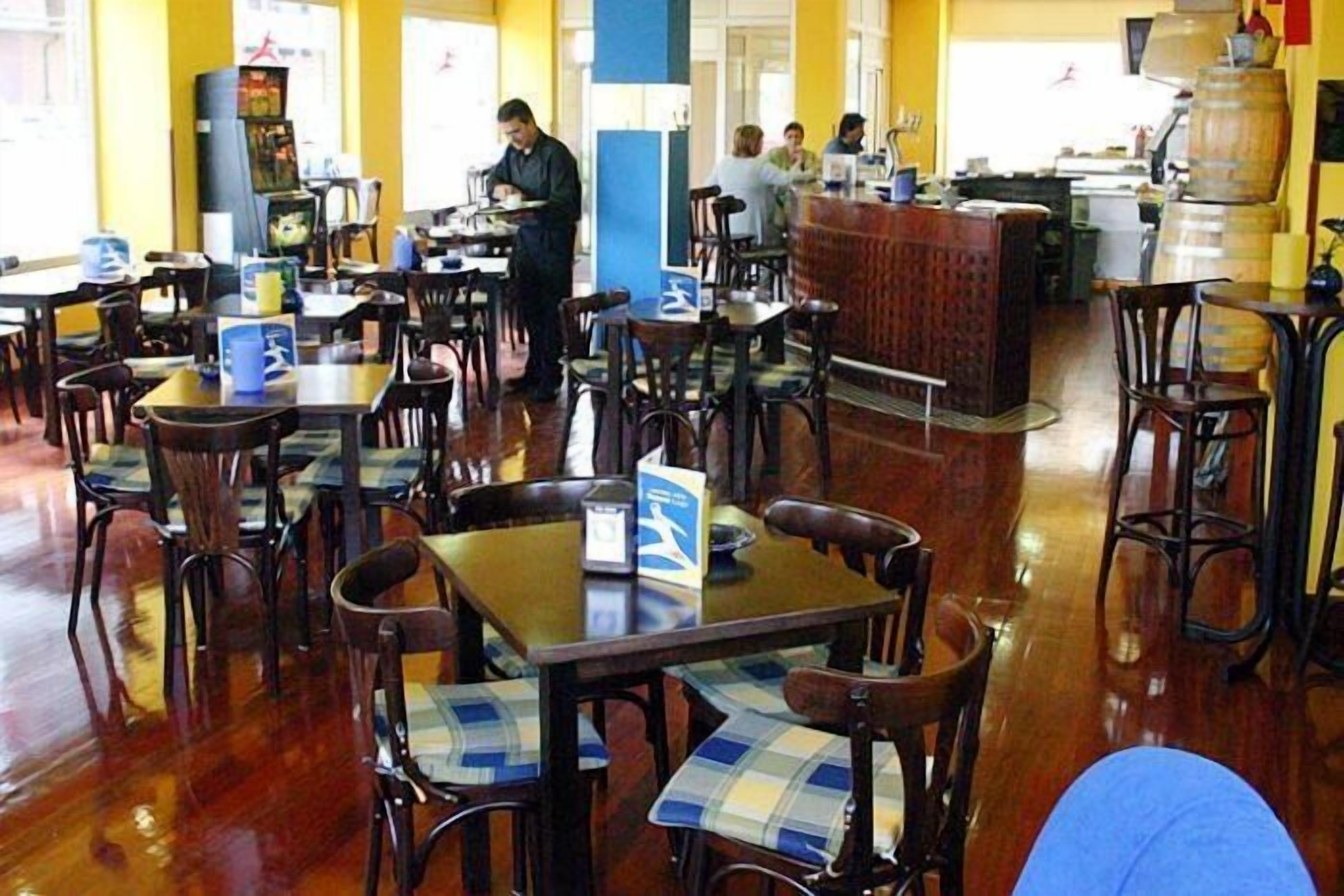 A restaurant with wooden tables and chairs, a bar area, and a kitchen in the background.