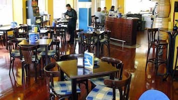 A restaurant with wooden tables and chairs, a bar area, and a kitchen in the background.