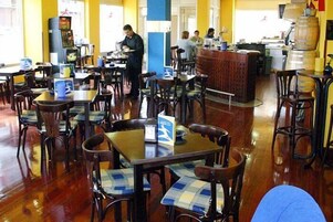 Un restaurante con mesas y sillas de madera, una zona de bar y una cocina al fondo.