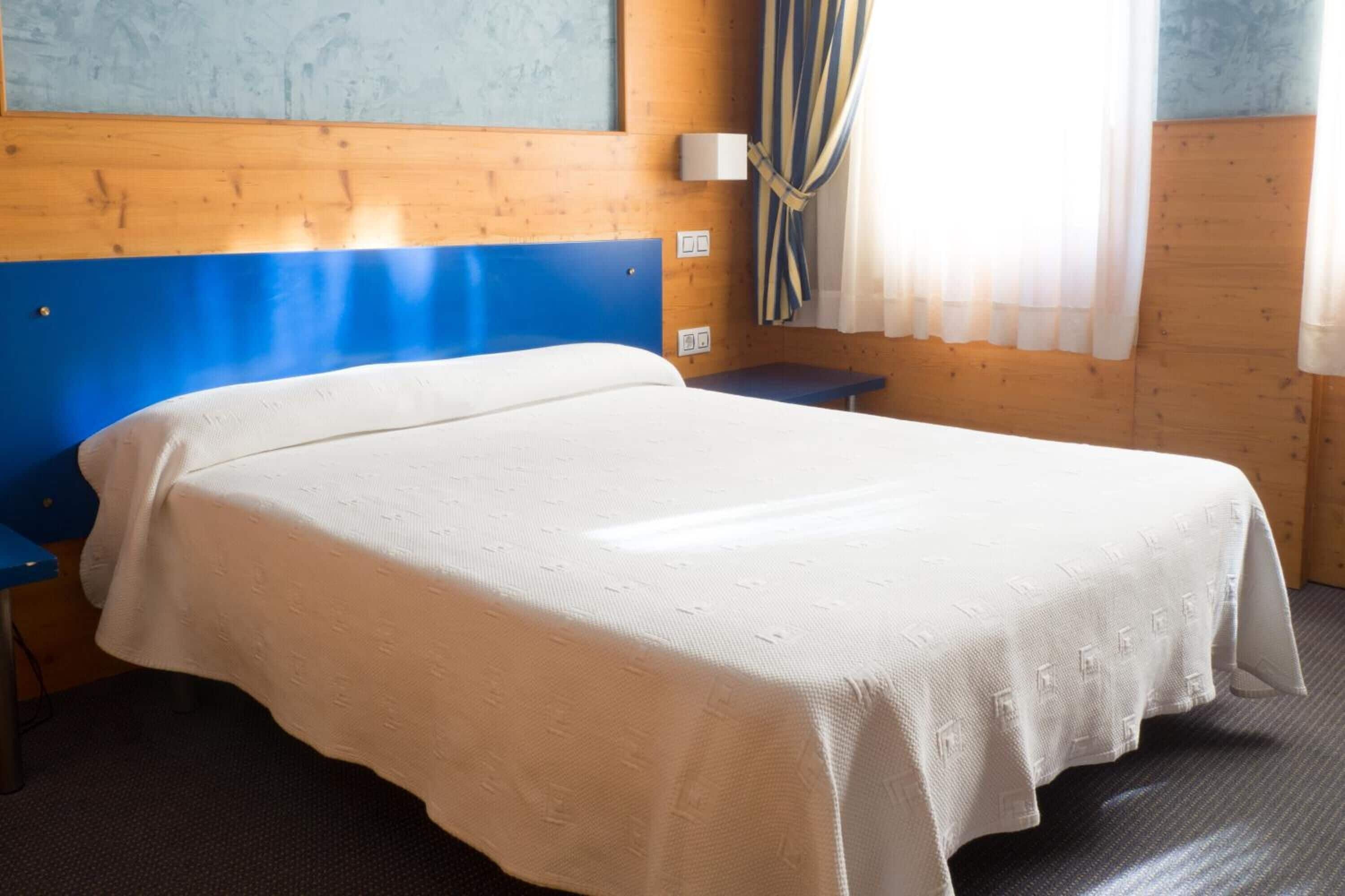Habitación individual con una cama, cabecera de madera, mesita de noche y ventana con cortinas.
