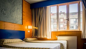 Habitación de hotel con dos camas, una ventana con cortinas, un radiador y vistas a edificios.
