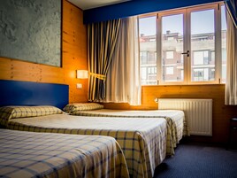 Habitación de hotel con dos camas, una ventana con cortinas, un radiador y vistas a edificios.