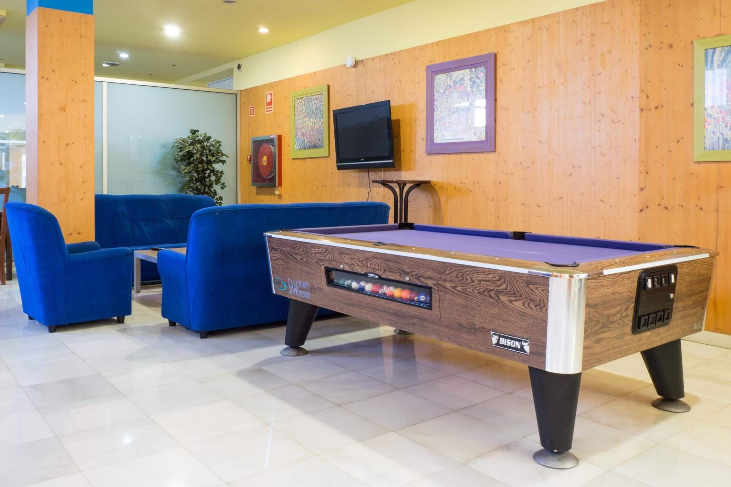 Una mesa de billar con el logotipo Bison, sillas azules, un televisor y obras de arte enmarcadas en la pared.
