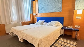 A hotel room with a large bed, a wooden headboard, a nightstand, a telephone, and a patterned rug.