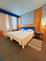 Habitación de hotel con una cama grande, cabecera de madera, mesita de noche, teléfono y una alfombra estampada.