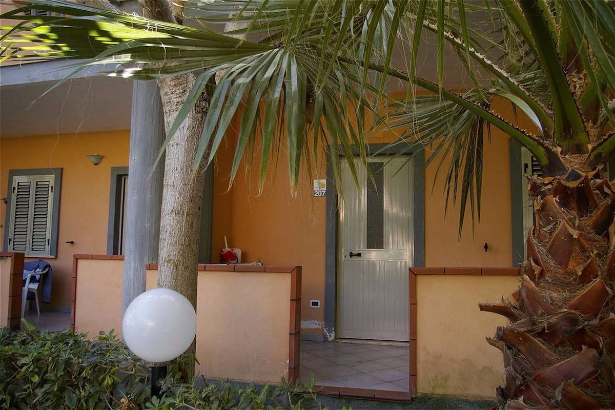 A building entrance with a palm tree, a door, and a number sign.