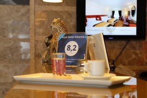 A reception area with a cheetah statue, a sign for Arya Hotel Sakarya, and a television displaying hotel rooms.