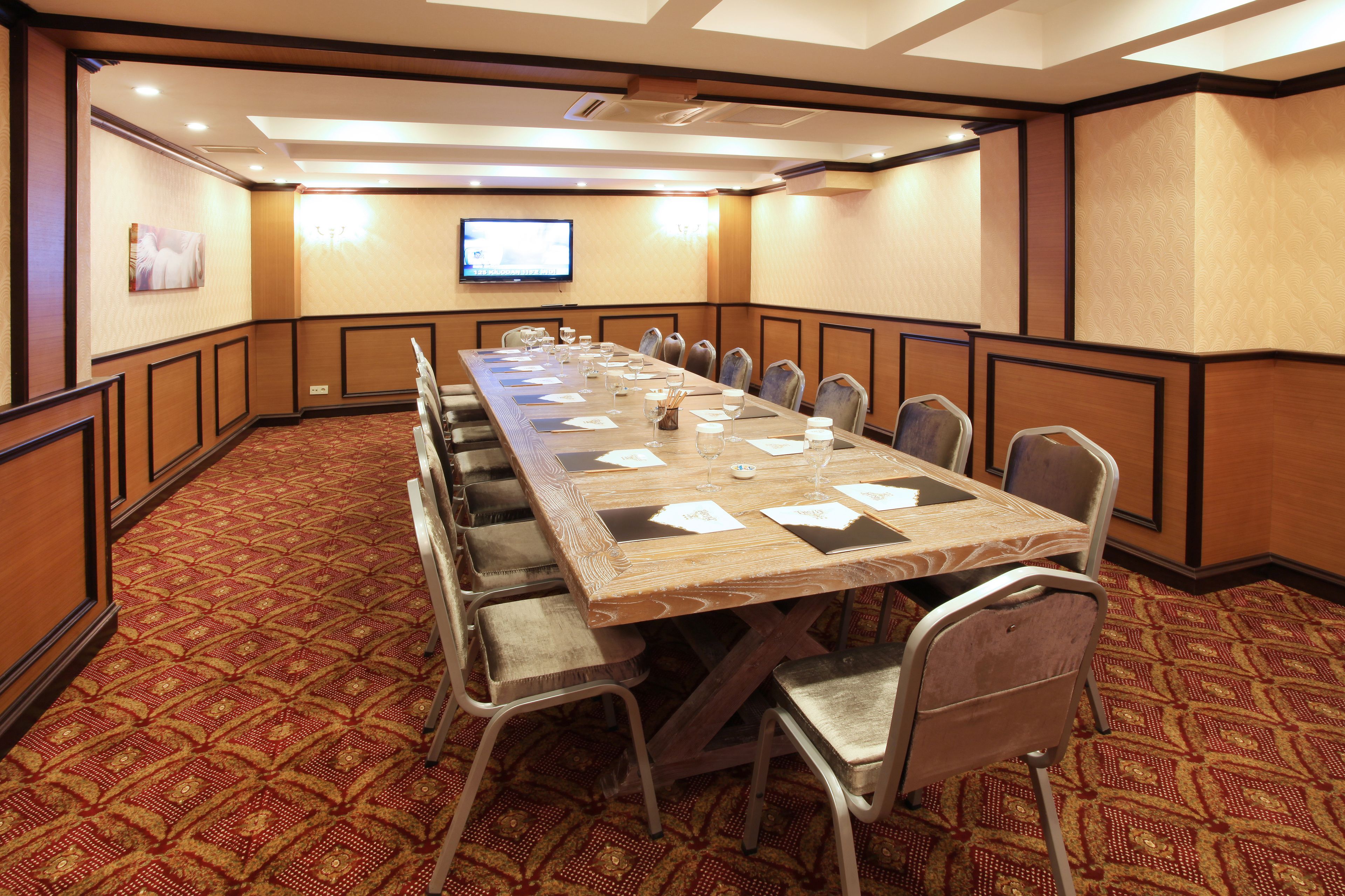 A conference room with a long table, chairs, a television, and patterned carpet.