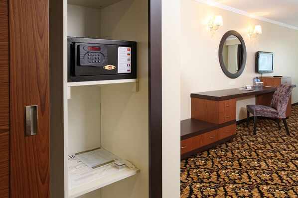 A hotel room with a wooden door, a minibar, a desk with a chair, a mirror, and a television. - Arya Hotel Business Deluxe (Adapazari)