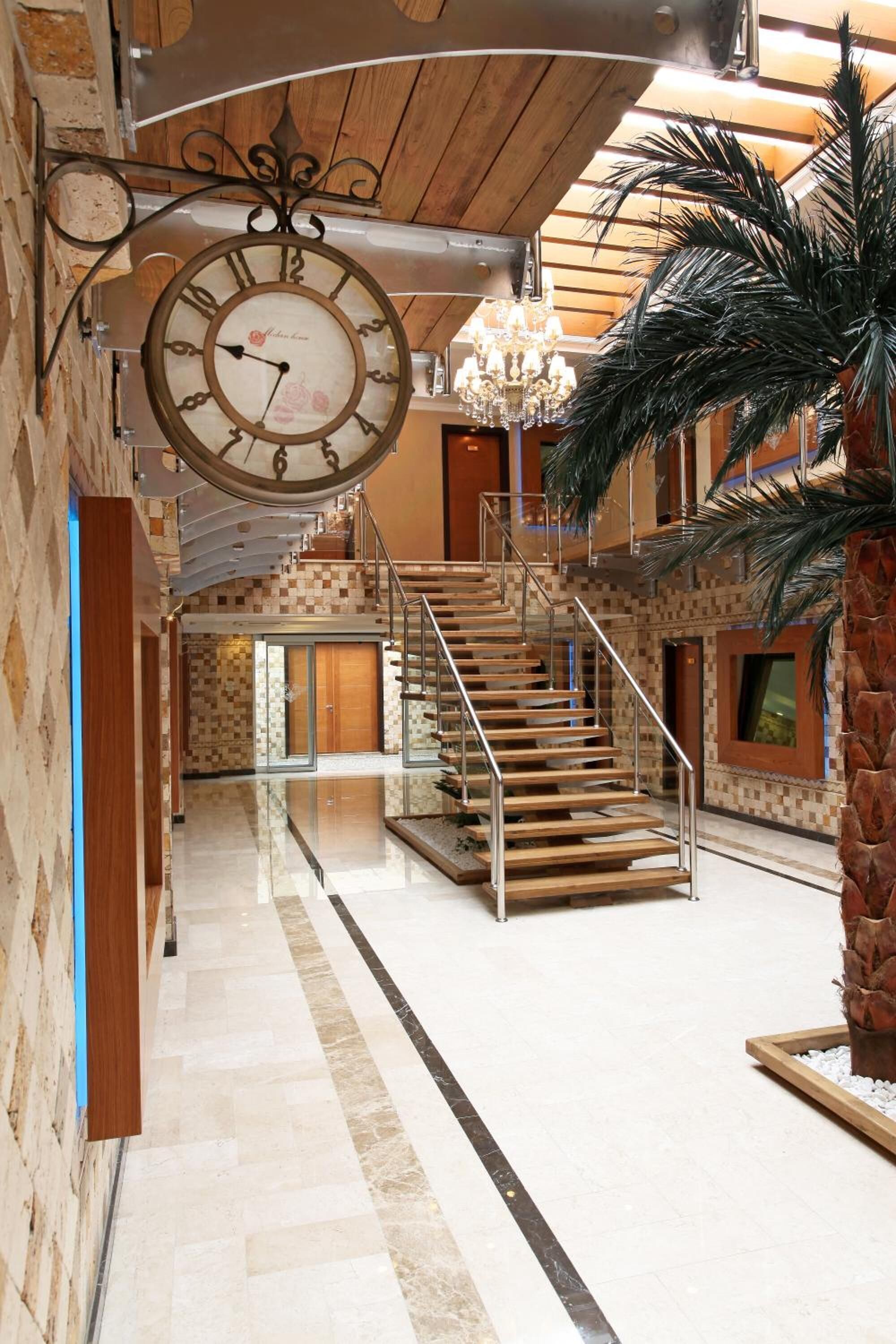 A spacious lobby with a large wall-mounted clock, a staircase, and a palm tree.