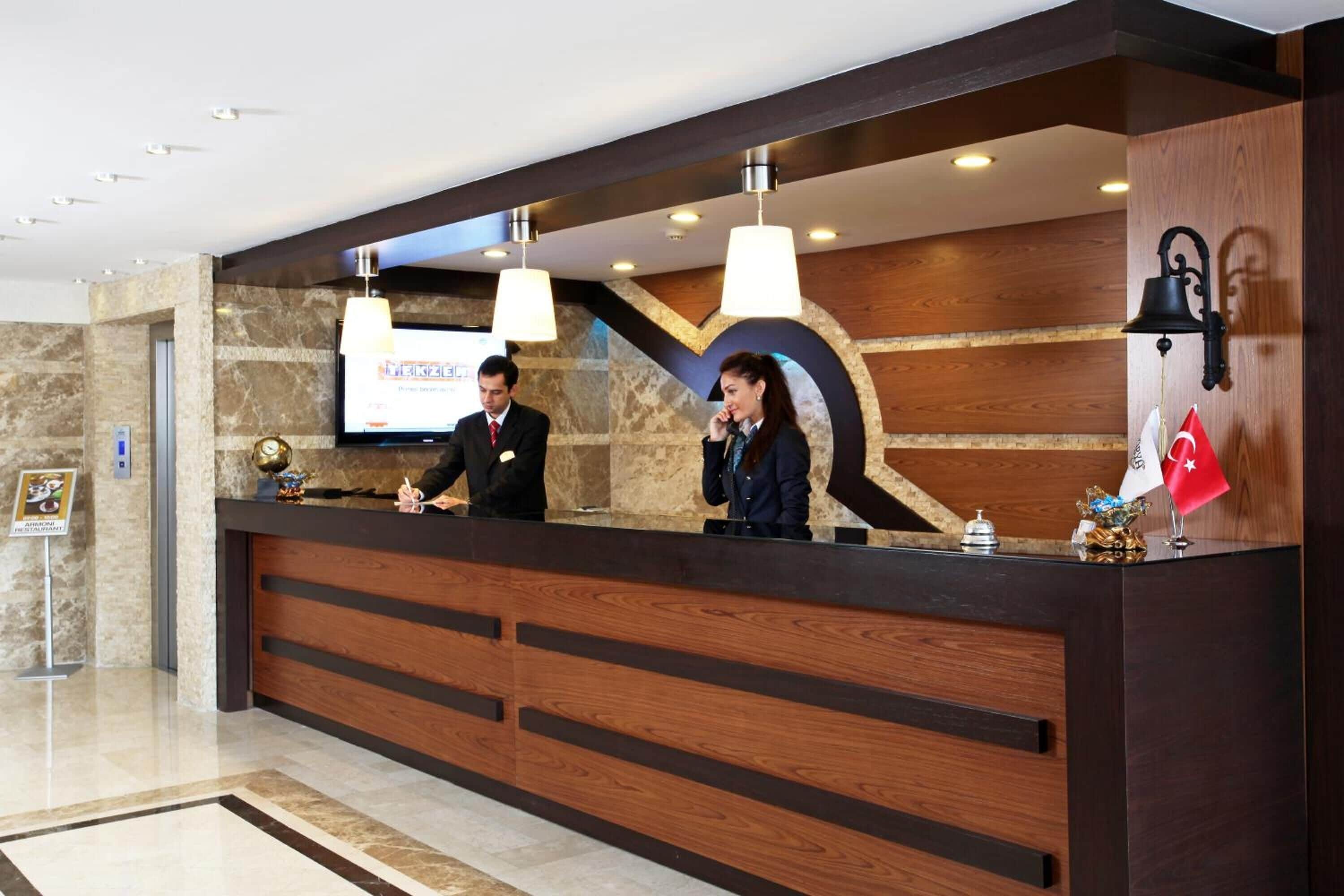 A reception desk with two staff members, a wooden panel design, and a flag.