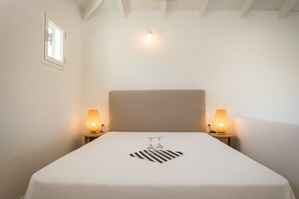 A neatly made bed with a striped pillow, two bedside lamps, and a small picture frame on the wall. - Neapoli Villas (Monemvasia)