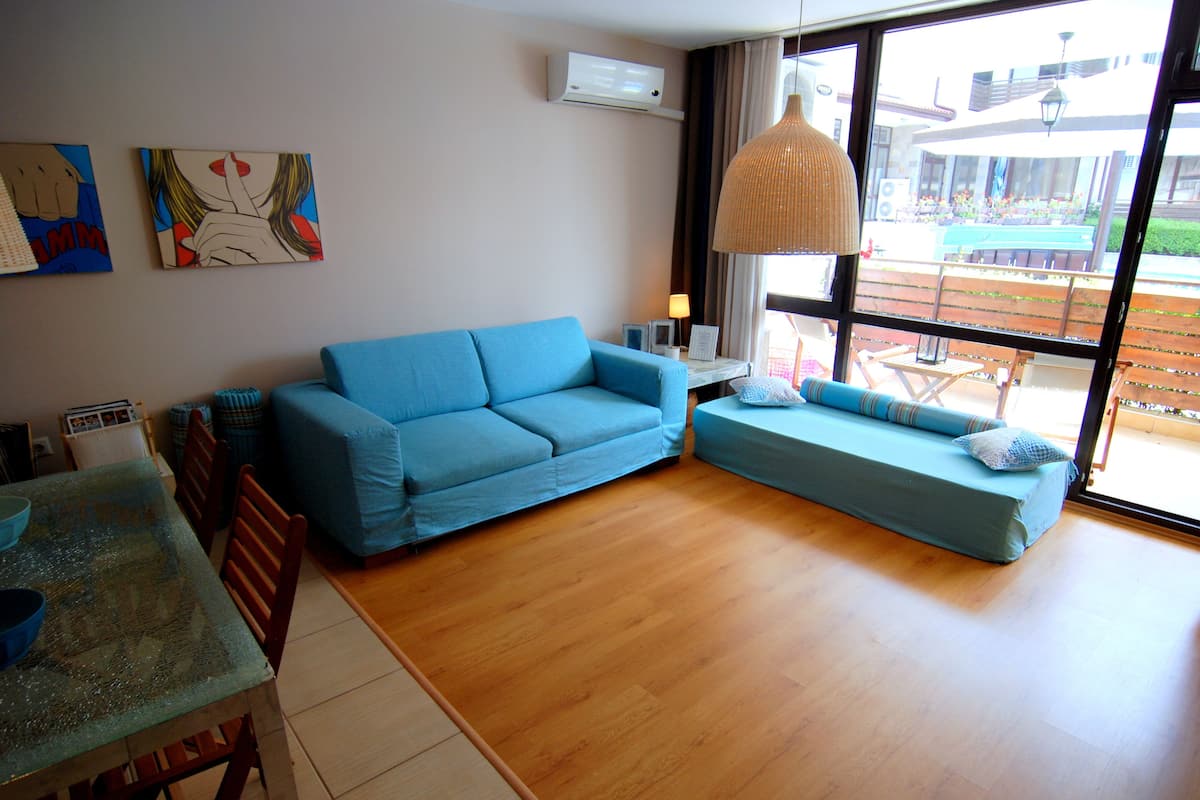Un salon avec un canapé bleu, un petit divan bleu et un coin repas comprenant une table et des chaises.