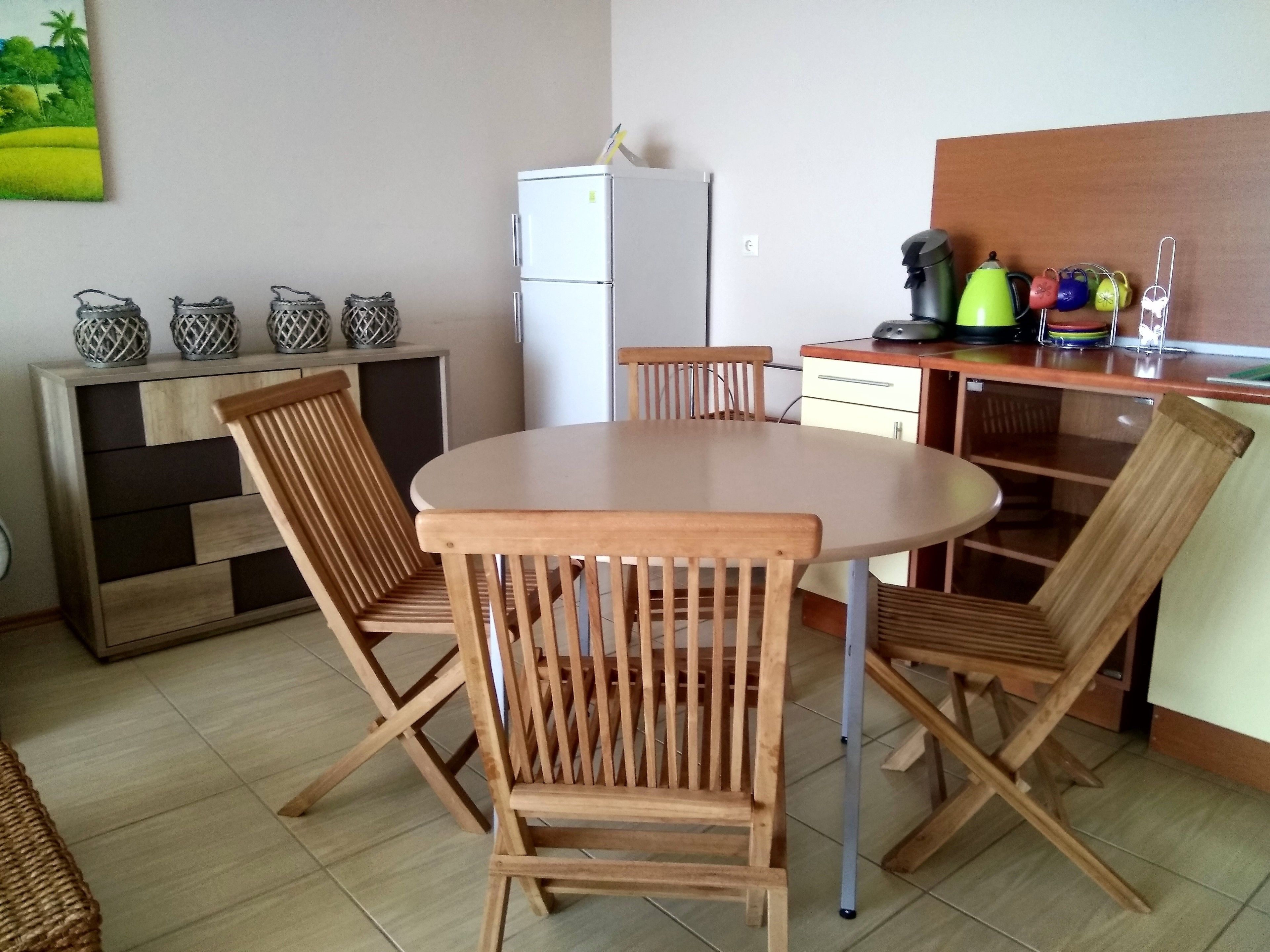 A compact kitchen with a round table and wooden chairs, a refrigerator, and a cabinet with decorative items.