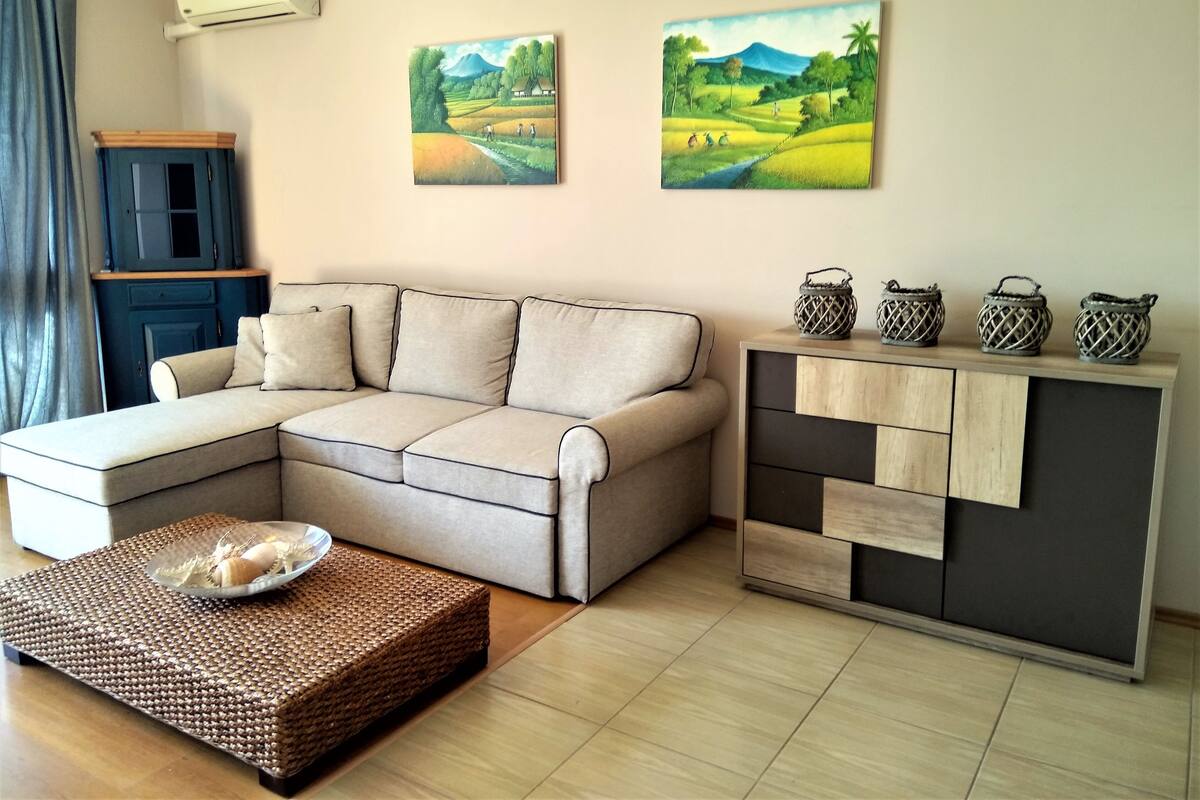 Un salon comprenant un canapé, une table basse et un meuble orné d’objets décoratifs. Deux tableaux sont accrochés au mur.