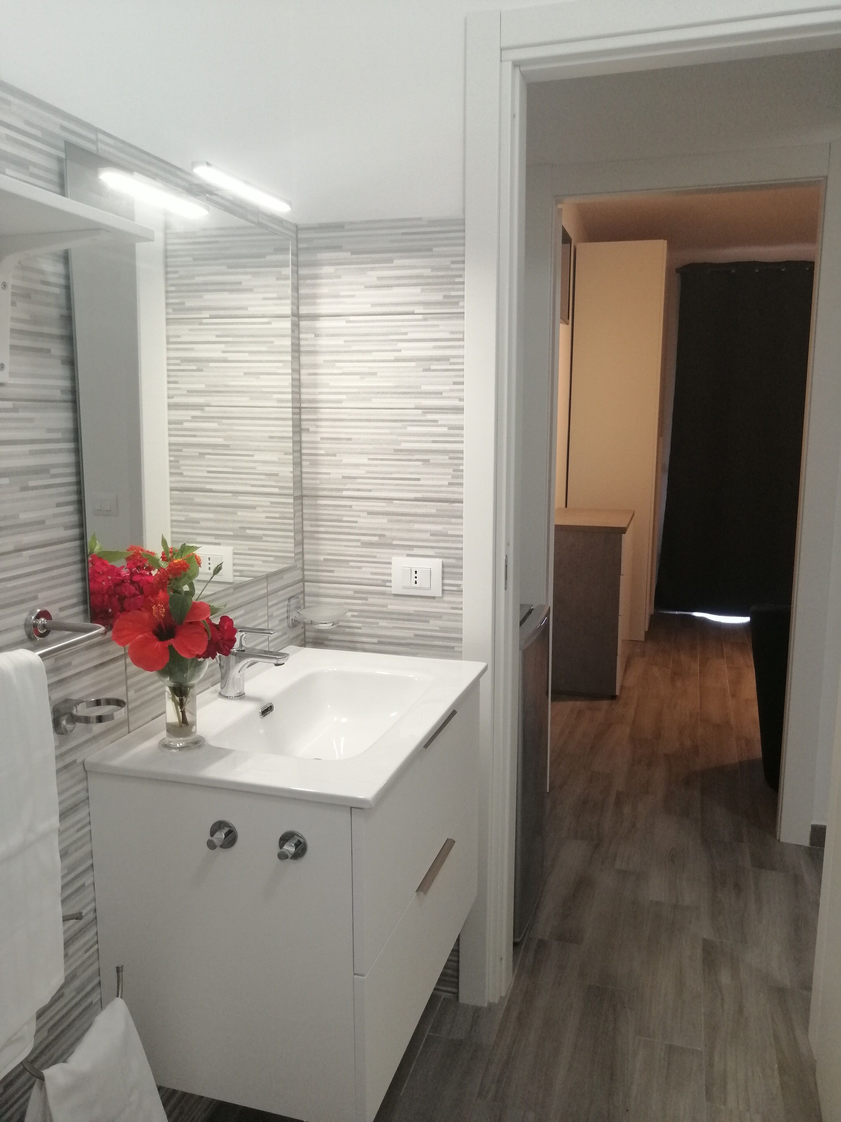Un baño moderno con un tocador blanco, un espejo grande y un jarrón de flores rojas.
