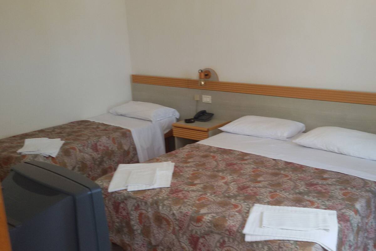 Une chambre d’hôtel avec deux lits simples, un petit bureau avec un téléphone et une télévision.