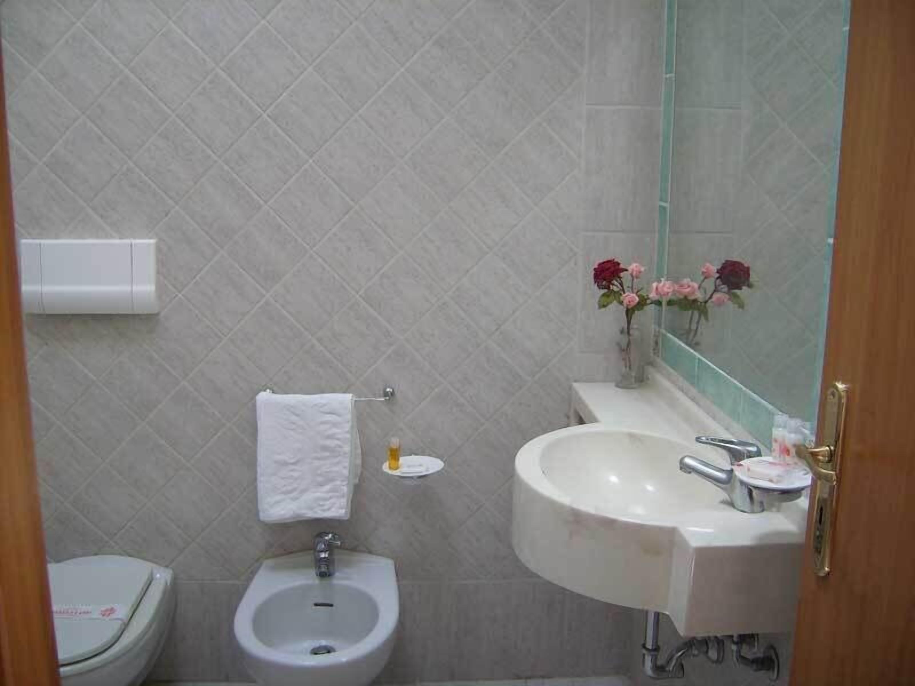 A bathroom with a bidet, a sink, a mirror, and a vase with flowers.