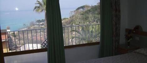 Un dormitorio con un balcón amplio, una cama y vista al océano.