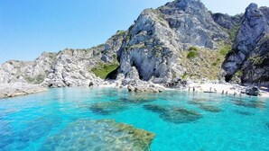 Un mar turquesa transparente con acantilados rocosos y una playa de arena.