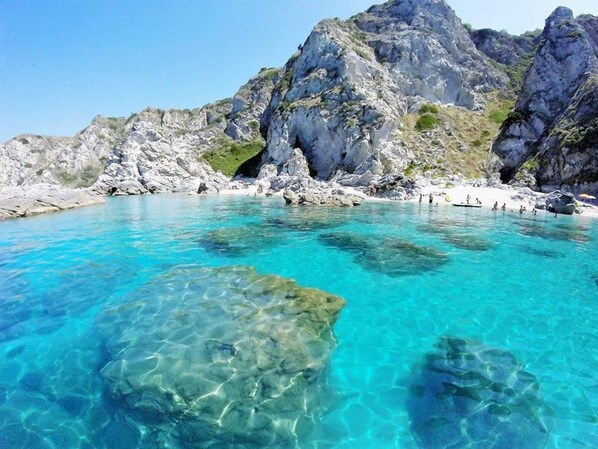 A clear turquoise sea with rocky cliffs and a sandy beach.