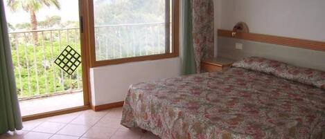 A bedroom with a bed, a window with a view of greenery, and a balcony with a railing.