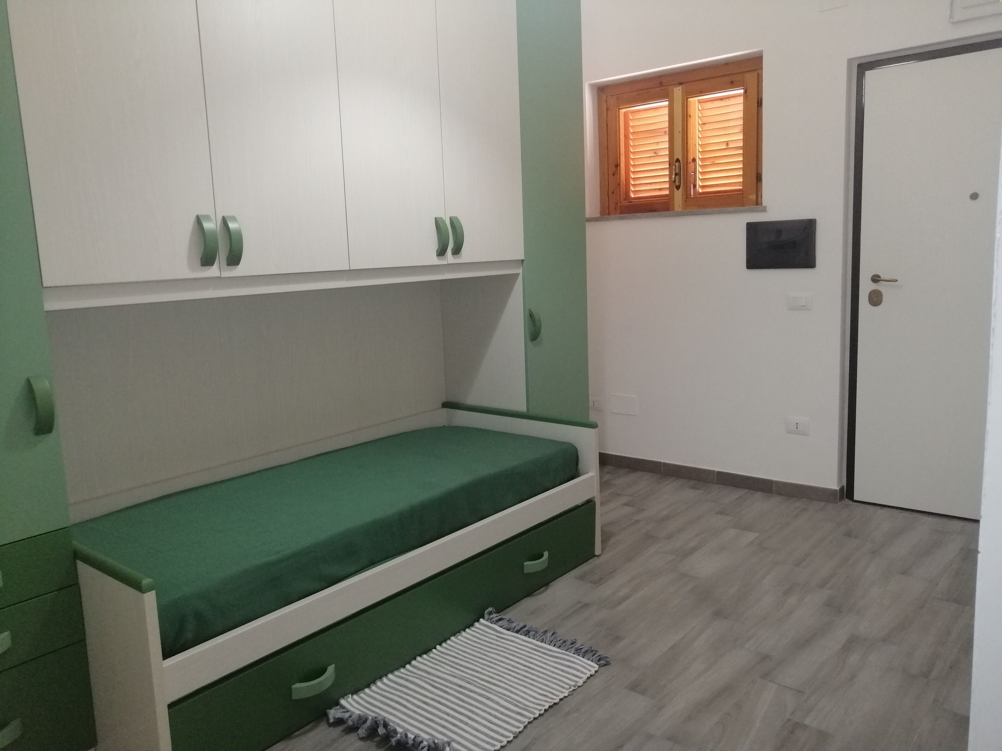 A room with a bed, a wardrobe, a window, and a door.