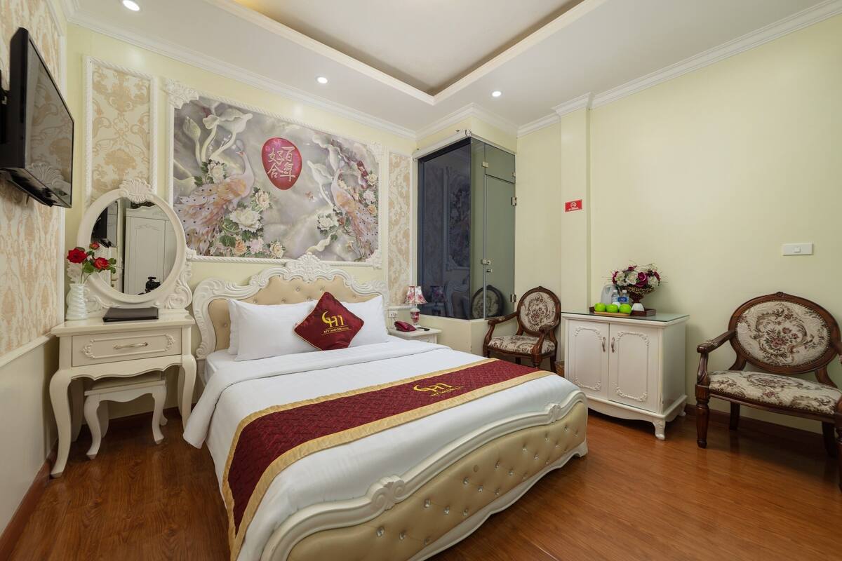 A well-appointed bedroom with a large bed, a dresser, a vanity with a mirror, and a television mounted on the wall.
