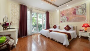 Une chambre d’hôtel avec deux lits, un lustre, un tableau et une vue à travers les portes vitrées.